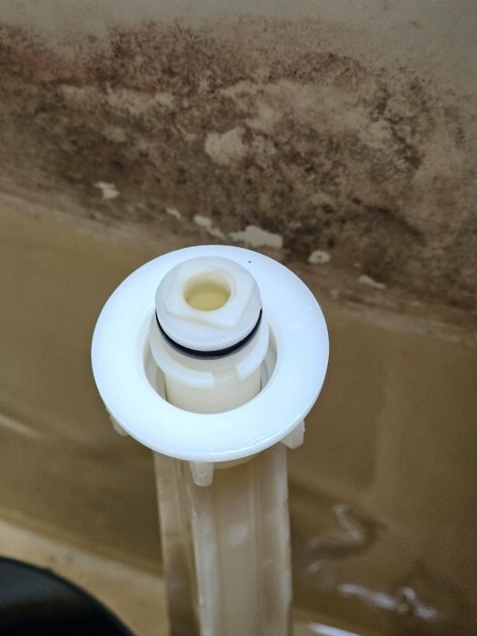 Plastmutter på en inloppsventil till en IFÖ Cascade toalett mot en bakgrund av kakel.