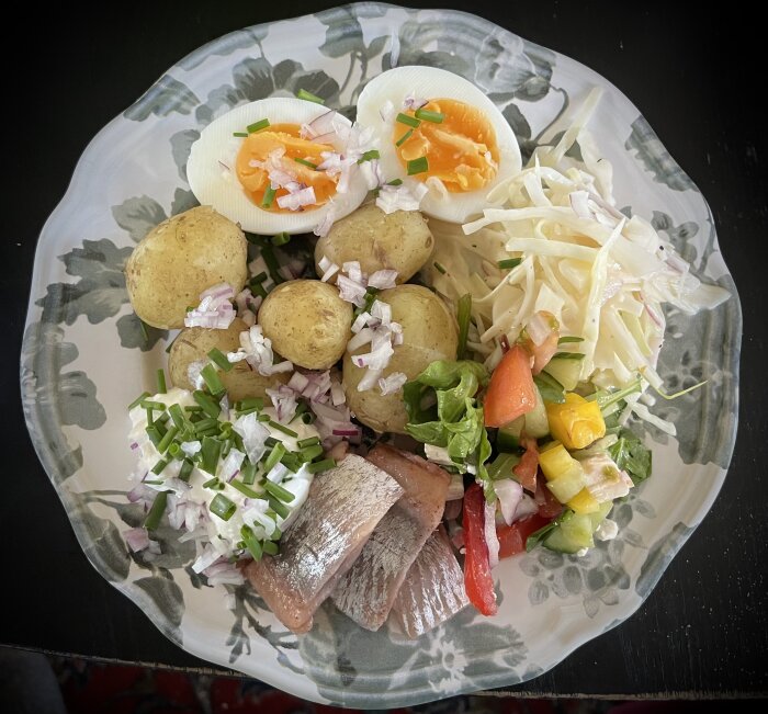 Tallrik med matjessill, färskpotatis, ägg, sallad, gräddfil, rödlök och gräslök.