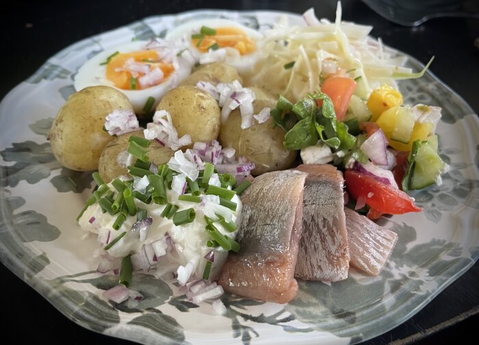 Tallrik med matjessill, färskpotatis, ägg, sallad, rödlök, gräddfil och gräslök.