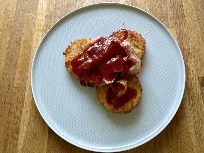 Hemlagade potatisbullar och bacon toppade med lingonsylt på en vit tallrik.