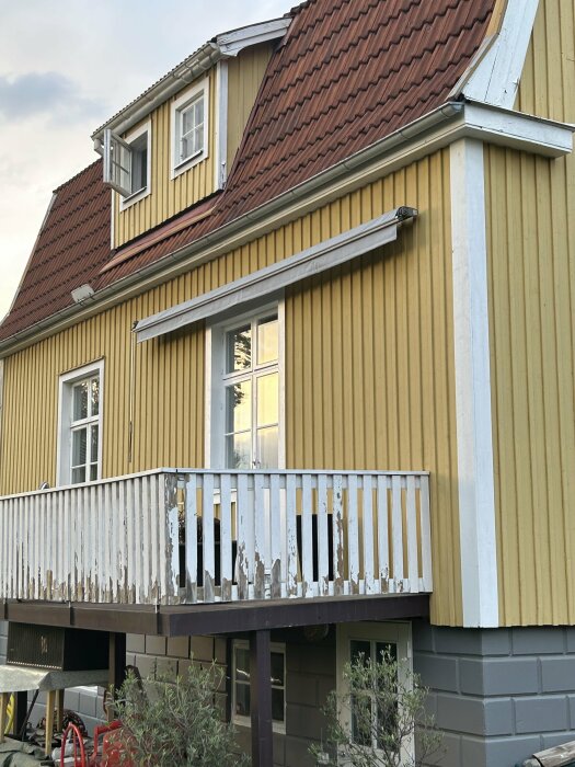 Delvis flagande vitmålad balkong på ett gult hus med grå grund från 1926, övervägande fasadfärg på räcke.