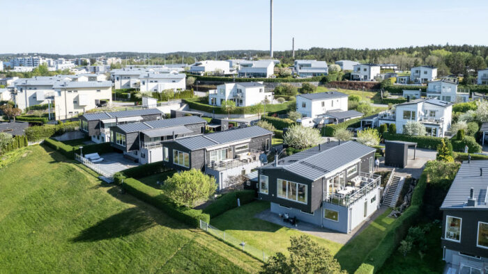 Vy över moderna radhus med enkel design i grönområde, med trädgårdar och terrasser.