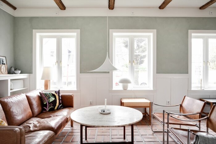 Stilfullt vardagsrum med skinnsoffa, designlampa och vit panelvägg som ger en dansk känsla.