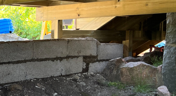 Ojämnt lagda betongblock i en mur under konstruktion med synlig sluttande mark och byggmaterial.