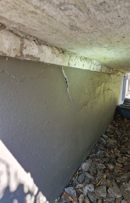 Sprucken grundfasad under trappa på ett 70-talshus med tecken på vattenskador och förfall.
