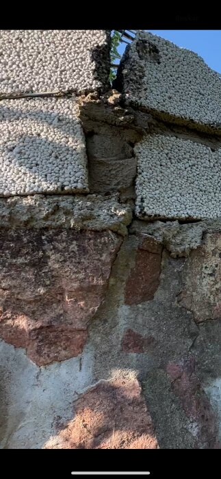 Ojämnt lagd stenmur med oregelbundna och spruckna cementfogar, möjlig felaktig byggnation.