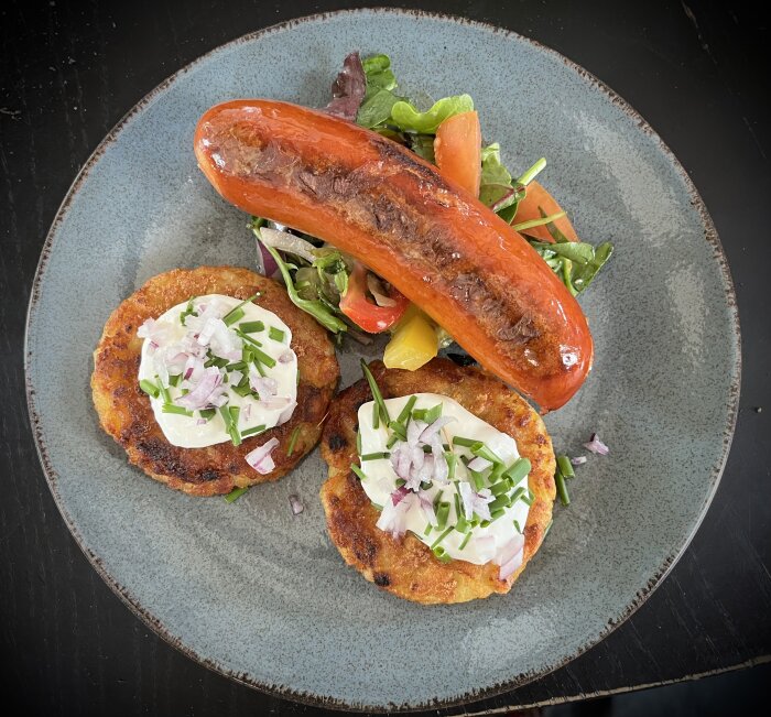 Potatisbullar med gräddfil och rödlök, kabanoss och sallad på en blå tallrik.