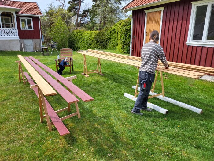 Person förbereder fasadrenovering genom att olja plankor framför röd trähusvägg med ny dörr och utan panel.