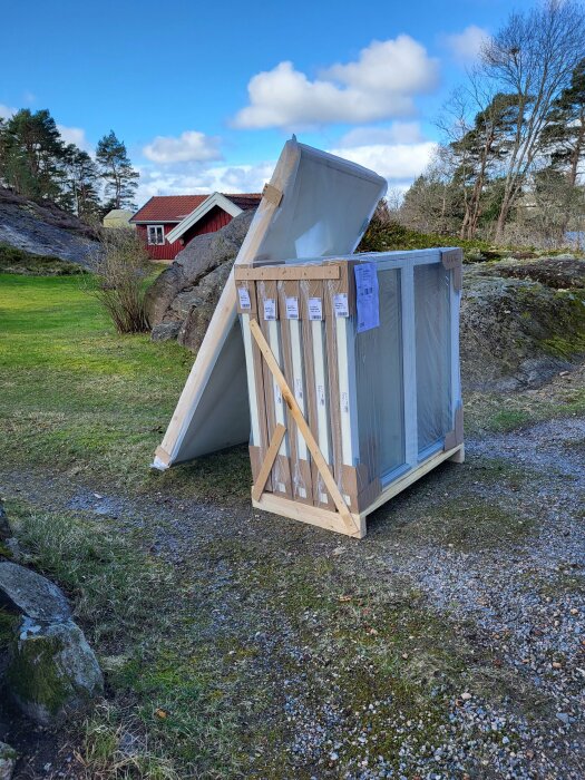 Nytt fönster paketerat och klart för installation med träram och skyddsplast, levererat i trädgård på en solig dag.