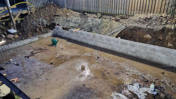 Pågående grundarbete med nygjuten betong och uppsatta murblock vid en byggarbetsplats.