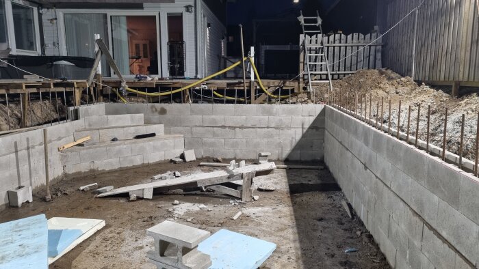 Pågående bygge av grundmur i betongblock med byggnadsmaterial och verktyg vid en bostad.