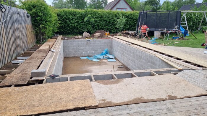 Grundkonstruktion av betongblock för byggprojekt med träplankor och byggmaterial i trädgård.