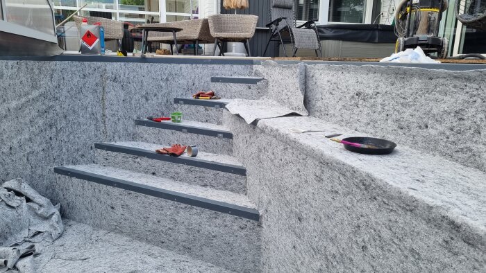 Installation av gråa stentrappsteg utomhus med verktyg och byggmaterial synliga.