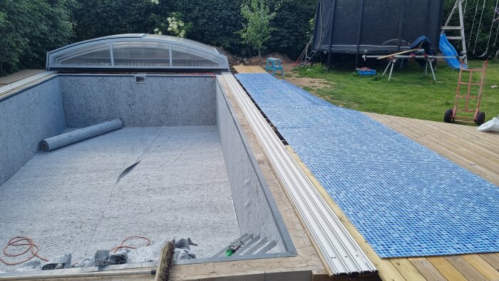Installation av pool med öppet skjutbart tak och delvis färdiglagd trätrall.