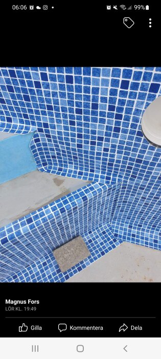 Blå mosaikklädda trappsteg i en pool, delvis fylld med vatten.