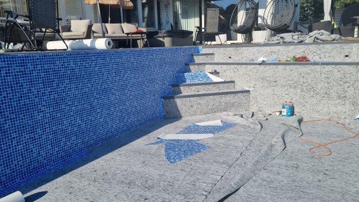 Pool under renovering med blå mosaikplattor och oulagda plattor på betongtrappor.