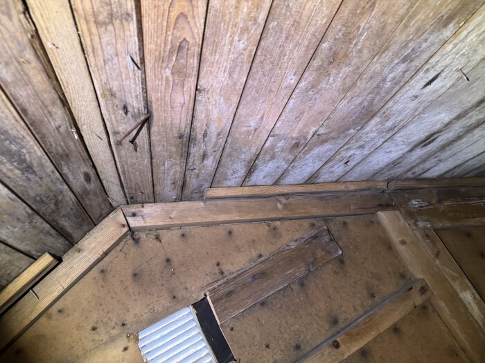 Takstruktur med träbjälkar och spikar, synlig från insidan av en byggnad, med en del av en stegstege.