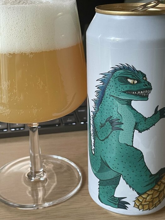 Ölglas fyllt med grumlig New England IPA och en burk med illustration av en varelse som liknar Godzilla.