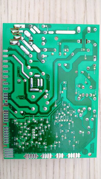 Kretskortets baksida med lödpunkter och spår, eventuellt från en diskmaskin, inga synliga brännskador.