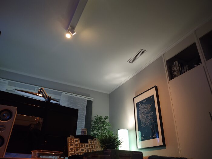Interiör av ett rum med takspots, högtalare, en ventilationsgaller och affisch på väggen.