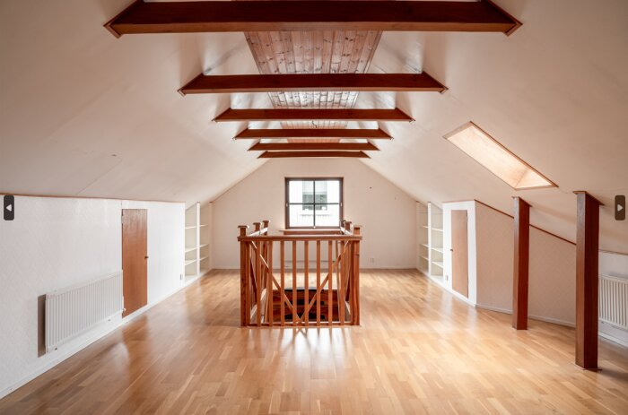 Interiör av oinredd vindsvåning med träbjälkar, parkettgolv och inbyggda fönster i taket.