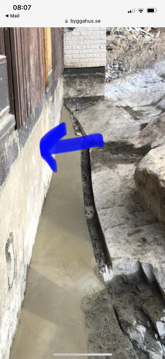 Grundmur med en blå pil som pekar på en potentiell läckplats, intill berg och nyasfalterat område.