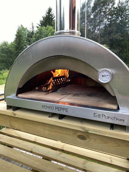 Vedeldad pizzaugn på en trädäckbänk med rostfria profiler och eld inuti ugnen.