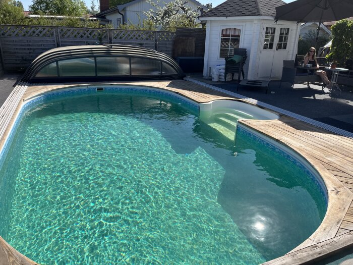 Renoverad pool med ny liner, rostskyddsmålad och omgiven av trädäck och utemöbler i soligt väder.