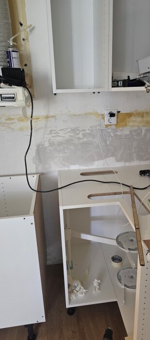 Omonterade köksskåp och överskåp i ett rum med lutande vägg.