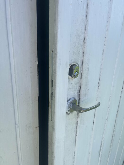 Vit dörr med borrade hål ovanför ett låshål och metallhandtag, tecken på DIY-underhåll.