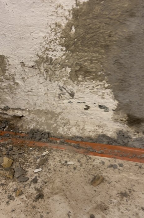Fuktfläckar på en vitmålad källarvägg med ett synligt smalt orange metallrör längs golvet.