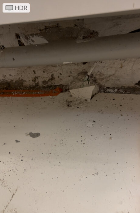 Smalt metallrör längs en skadad betongvägg, fuktfläckar synliga, rörbyteriets kontext.