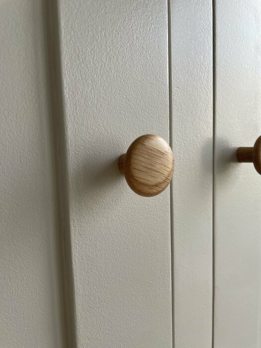 Närbild på en vit MDF garderobsvägg med en träknopp, del av ett DIY-projekt med Ikea stommar.