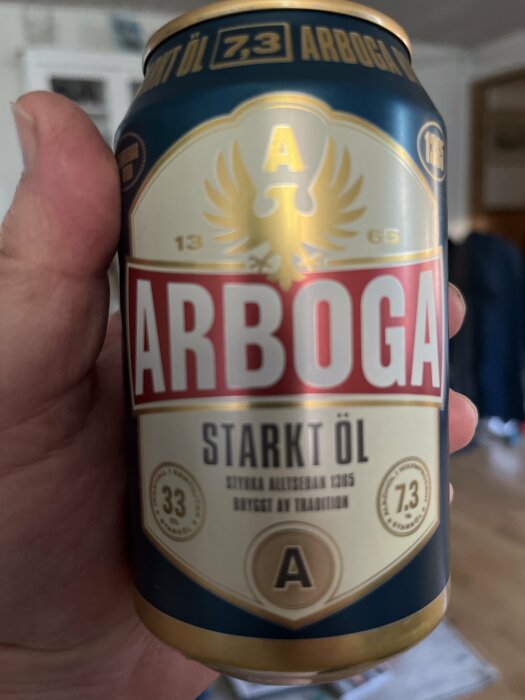 En hand håller en burk Arboga Starkt Öl med alkoholhaltsmarkeringen 7.3%.