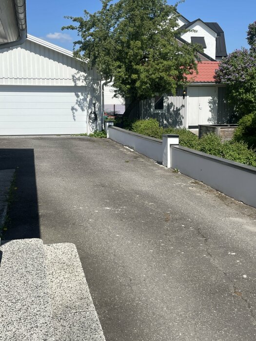 Lång vit stödmur av lecablock med sprickor i putsen längs uppfarten mot garage.
