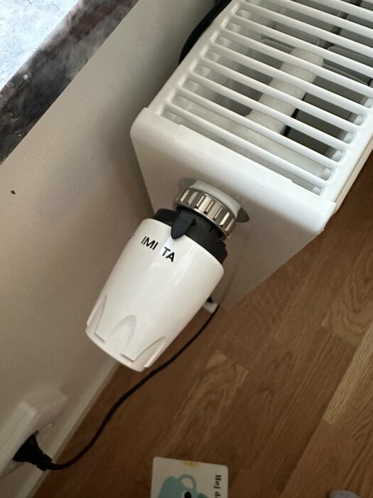 Termostat inställd mellan märkningarna IMI och TA på en radiator, tycks vara fast och ej justerbar.