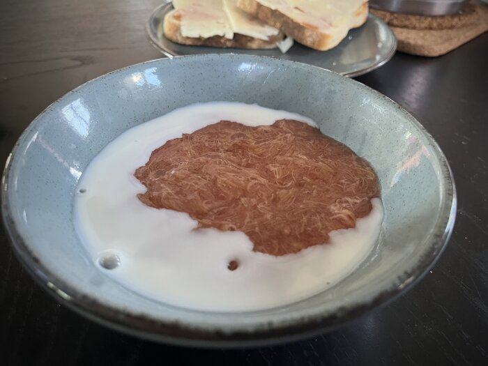 Nykokt rabarberkräm i skål med mjölk, bredvid en rostmacka med marmelad och ost.