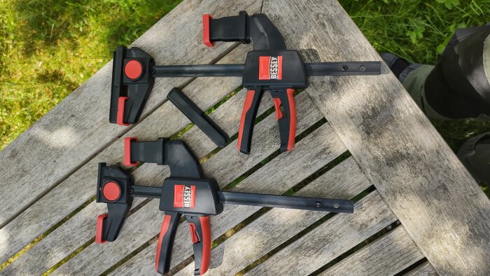 Bessey EZR15SET enhandstvingar i 2-pack, kompatibla med skensystem, på en träbänk.