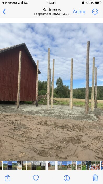 Grundläggning av ett utomhusprojekt med telefonstolpar som stödstrukturer på en lerig mark bredvid en röd byggnad.