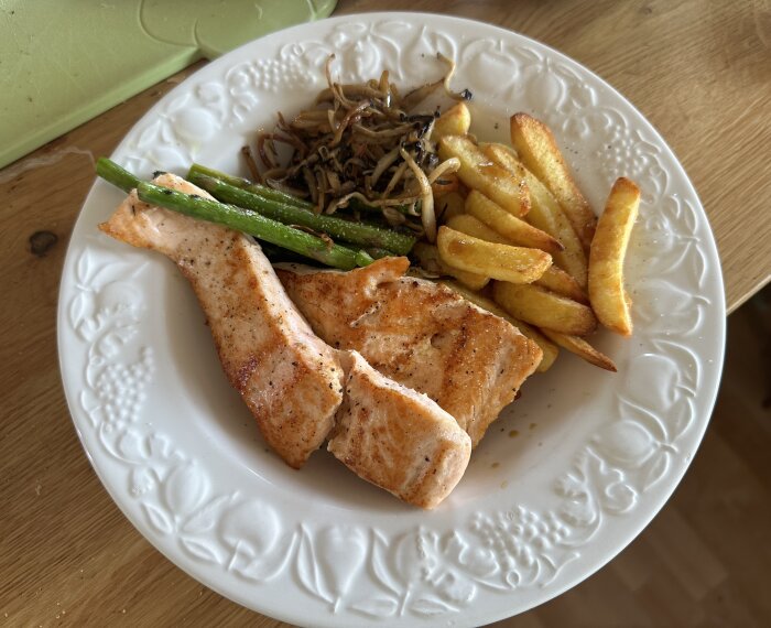 Tallrik med grillad lax, serverad med pommes frites, sparris och kungsmusslingar.