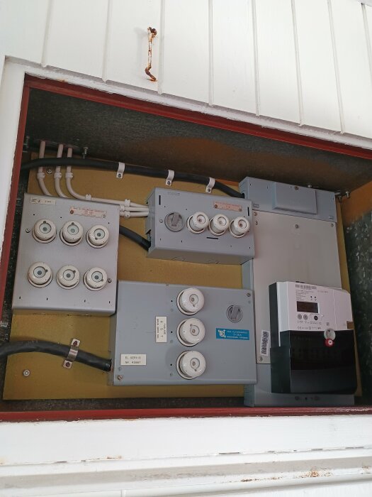 Gammalt proppskåp utan jordfelsbrytare i ett förråd, med synliga säkringar och kablar.