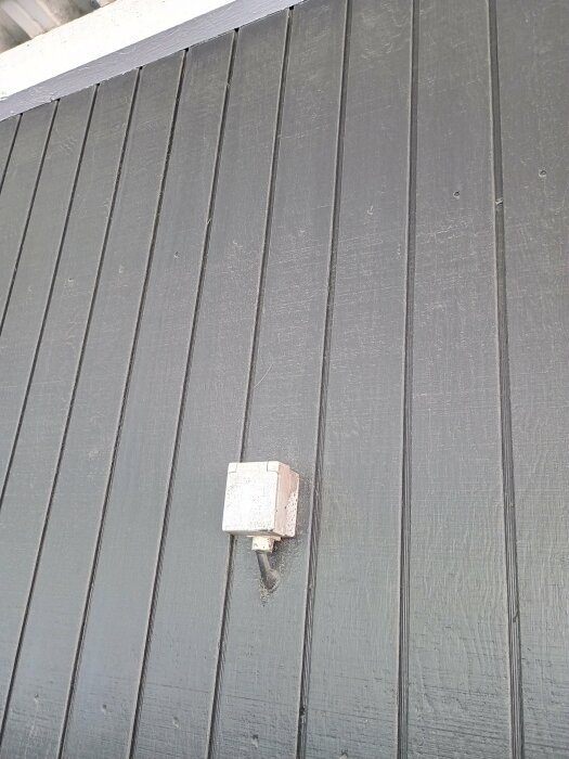 Gammalt eluttag på grå trävägg i carport, potentiell anslutning för poolpump.
