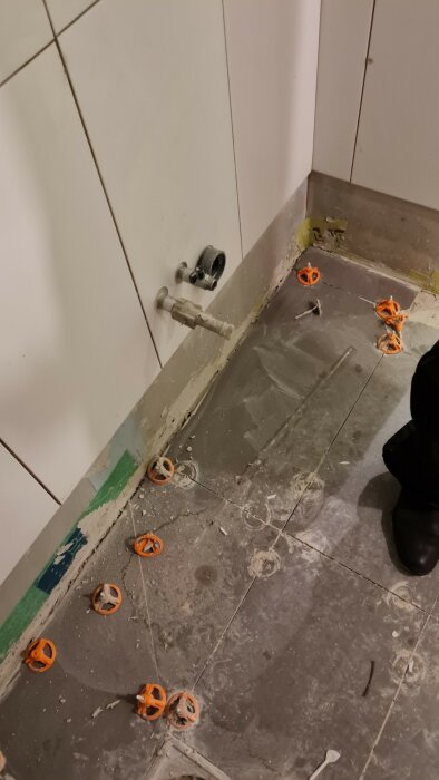 Hörn av ett badrum under renovering med kakel, synliga rör och spackelrester.