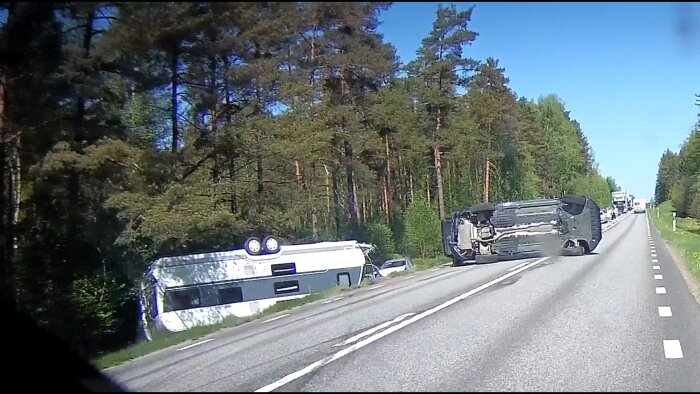 En vält husvagn och bil orsakar trafikstörning på landsväg omgiven av skog.