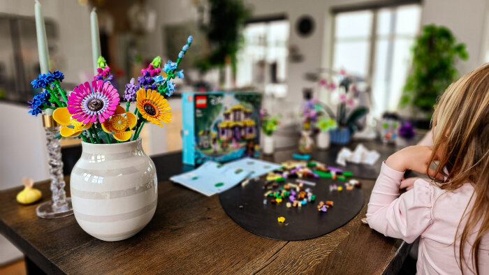 Blombukett av LEGO i vas bredvid en låda med LEGO Botanical Collection och ett barn som bygger.