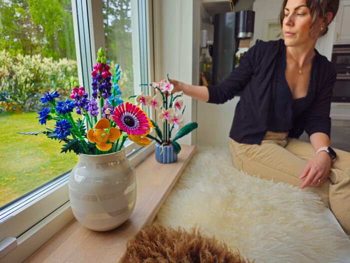 Kvinna bredvid fönster ordnar LEGO-blommor från Botanical-serien i vaser på en fönsterbräda.