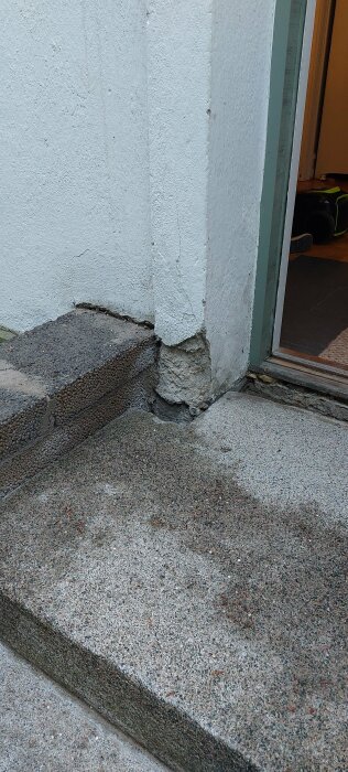 En trappa med ett glapp på 10 cm mellan betongstegen och husets vitkalkade vägg vid hörnet nära dörren.