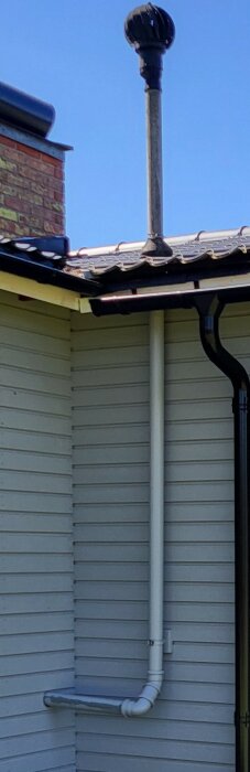 Ventilationsrör på husvägg för toalett med vindfläkt på tak och 90 graders böj nära marken.