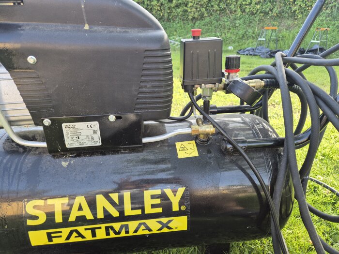 Kompressor med märkning 'STANLEY FATMAX' har oljespill och luftläckage, med synliga sladdar och kopplingar.