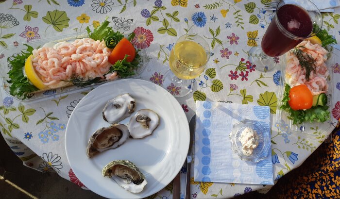 Bord med räkmackor, ostron och västkustsallad samt två glas dryck på ett blommigt duk.